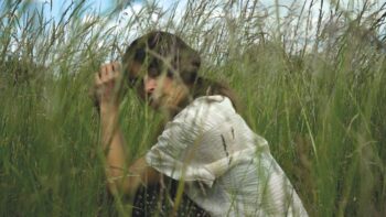 Claire is crouching eyes closed in the middle of very tall grasses which are taller than her in this position. She looks peaceful and immersed, totally in tune with natural world that she is part of.